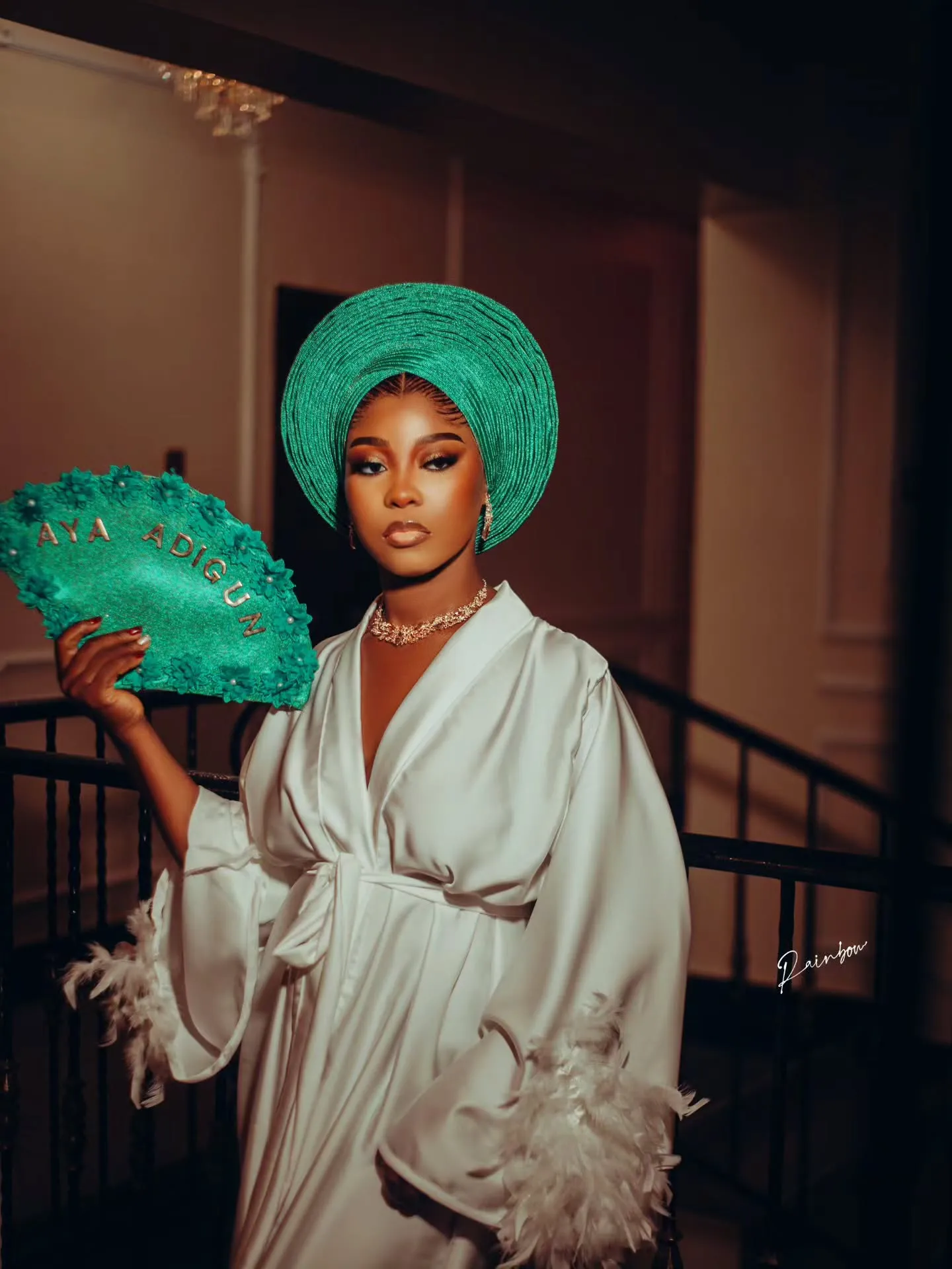 Bride in emerald gele and white robe fanning herself on the stairs