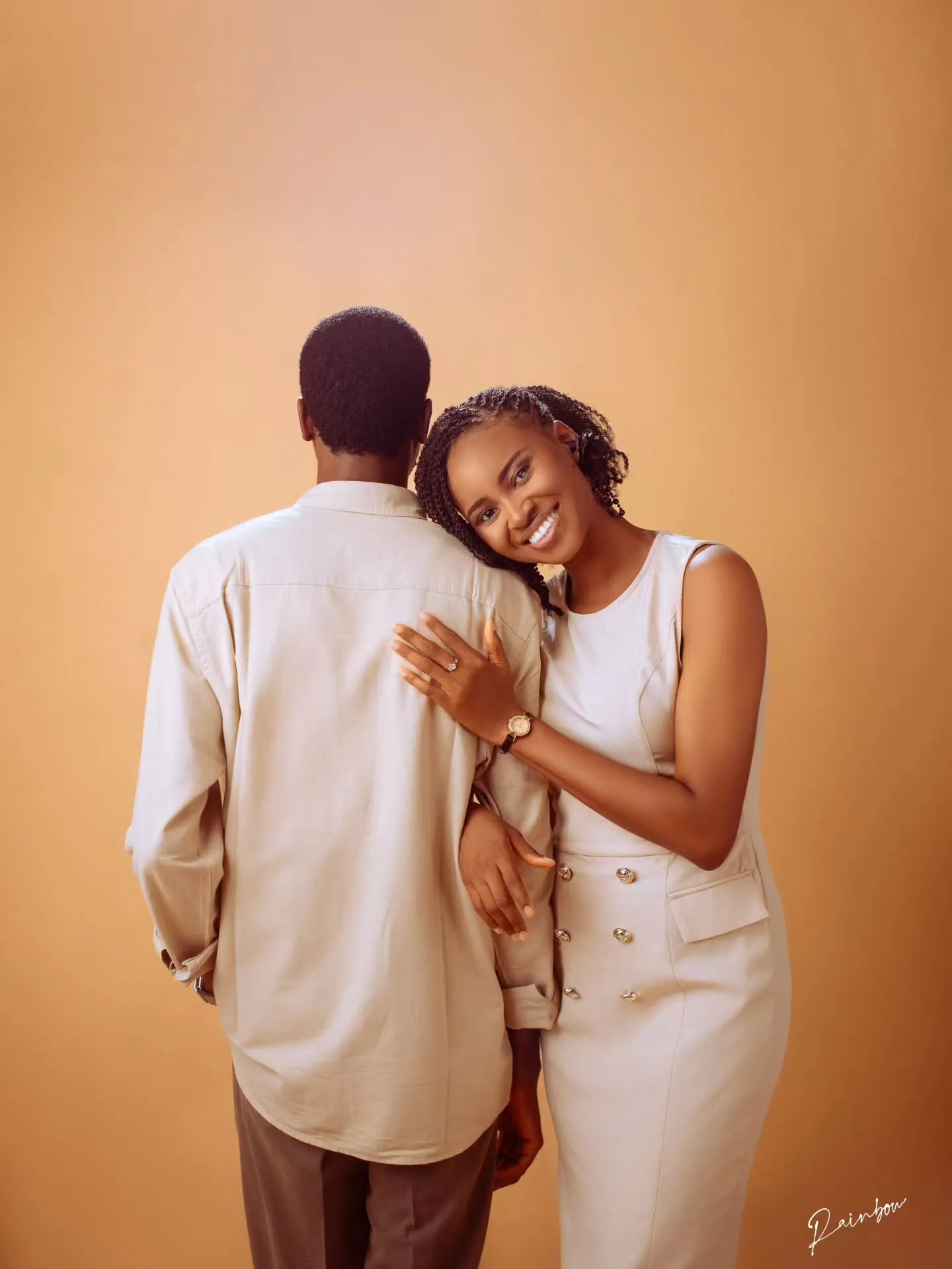 Couple in white leaning into each other on an amber backdrop