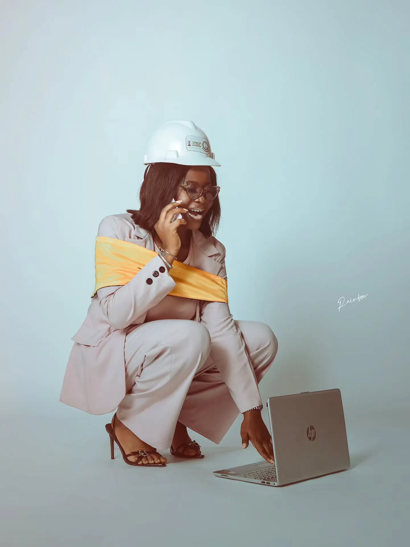 Graduate in a hard hat crouching beside a laptop