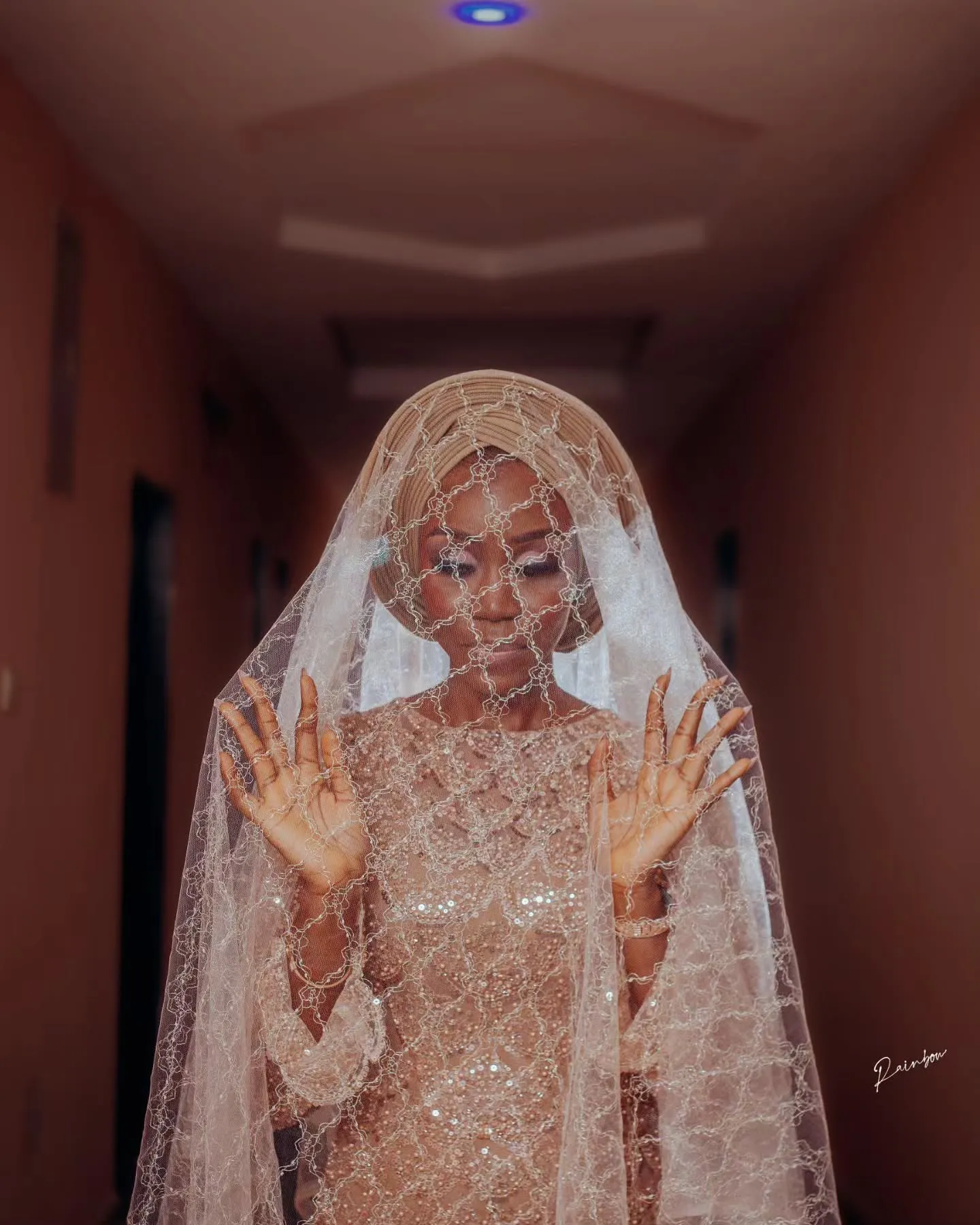 Veiled bride with hands raised in the hallway