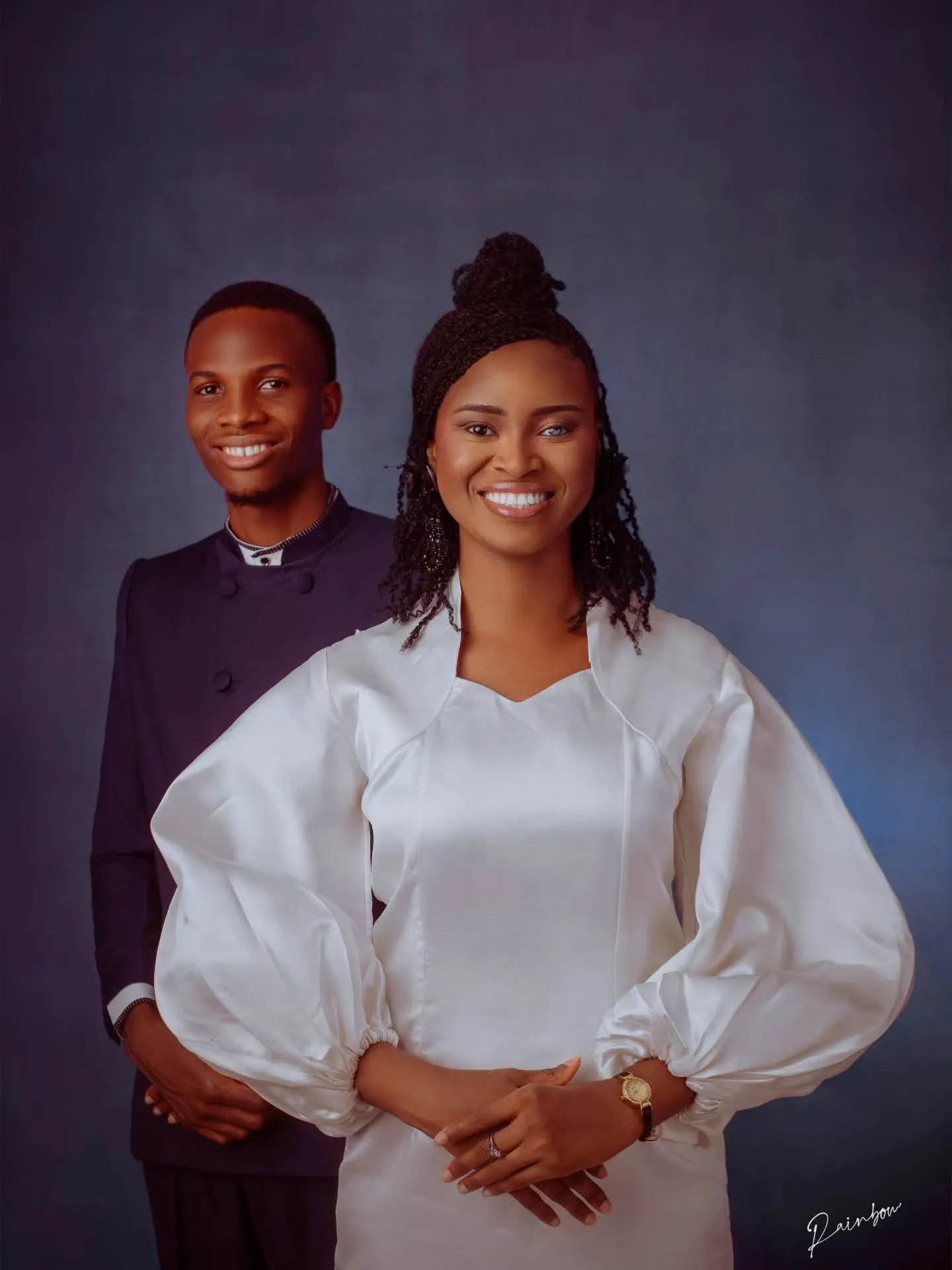 Couple in white smiling against a blue backdrop